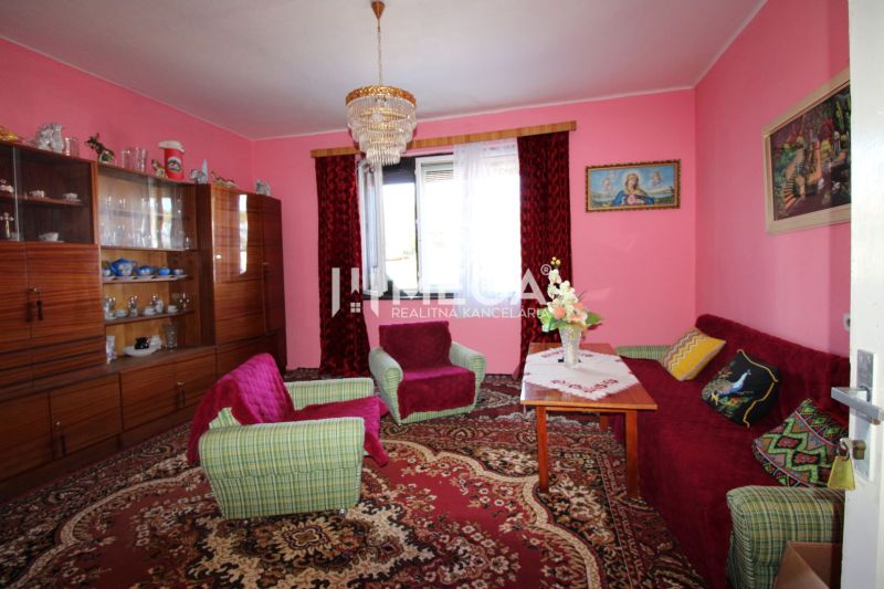 Living room with pink walls, a sofa set, a display cabinet, and a chandelier in a family house.