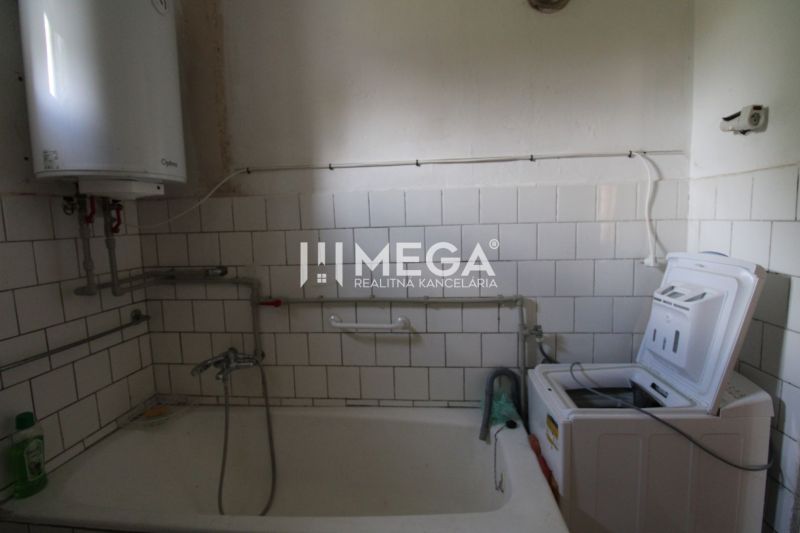 A bathroom in a family house with a bathtub and a washing machine, surrounded by white tiles.