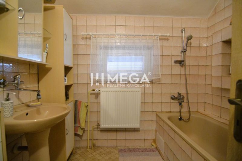 A bathroom in a family house with beige tiles, a bathtub, and a sink.