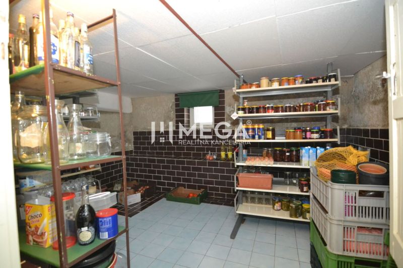 A pantry with shelves full of preserves in a family house, stone-clad walls, and a tiled floor.