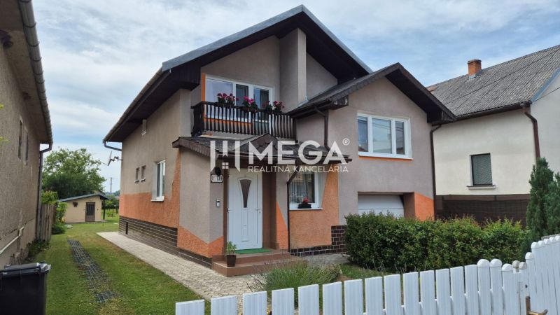 A family house in Lackovce with a balcony, surrounding greenery, and a white fence.
