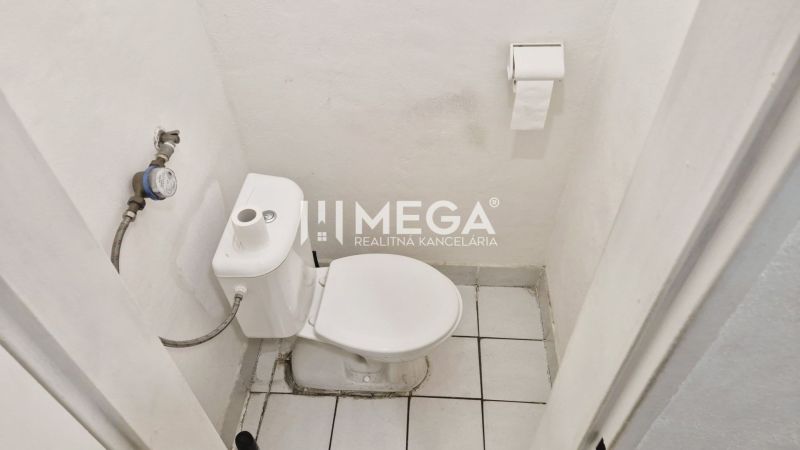 The restroom in the office with white walls and ceramic flooring.