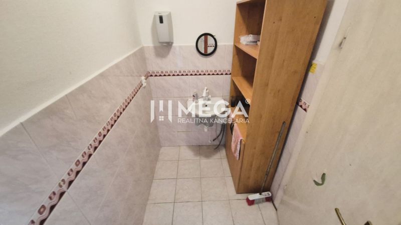 Bathroom in commercial premises with a sink, shelves, and tiled walls.
