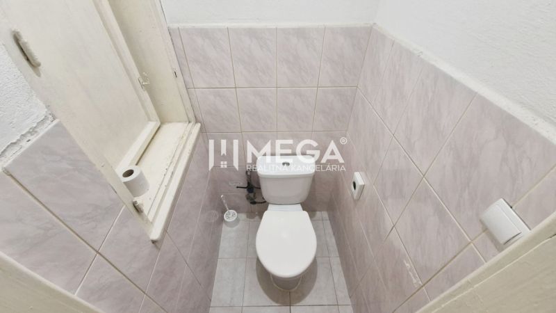 A restroom with walls lined with light tiles and a window in commercial premises.