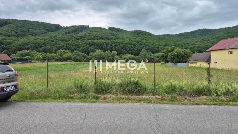 Lands - housing in Zubné, green meadows, fencing, car by the road, wooded hills.
