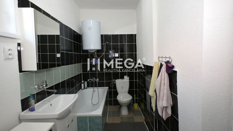 A bathroom in a family house with a bathtub, sink, and boiler, black and white tiles.