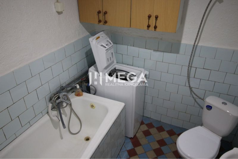 A bathroom in a family house with a bathtub, washing machine, and toilet, tiled.
