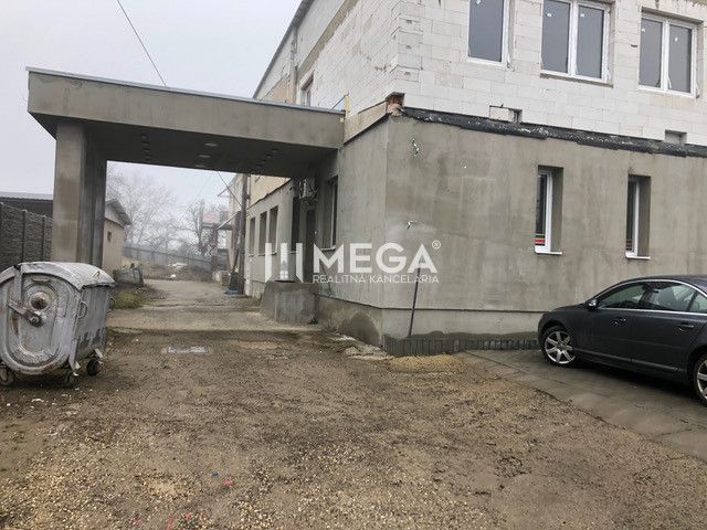 A building on SNP Street in Snina with a parked car and a container on a gravel surface.