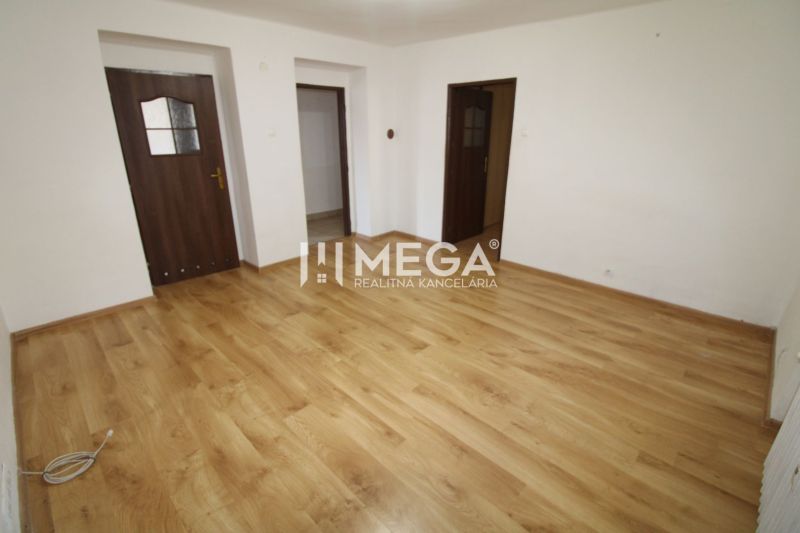 An empty room with white walls and a wood-patterned floor in a three-room apartment.