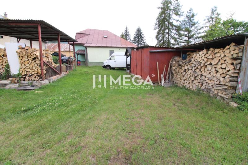 The courtyard of the family house in Ulič at Ulič 131, grass, stored wood, and a shelter.