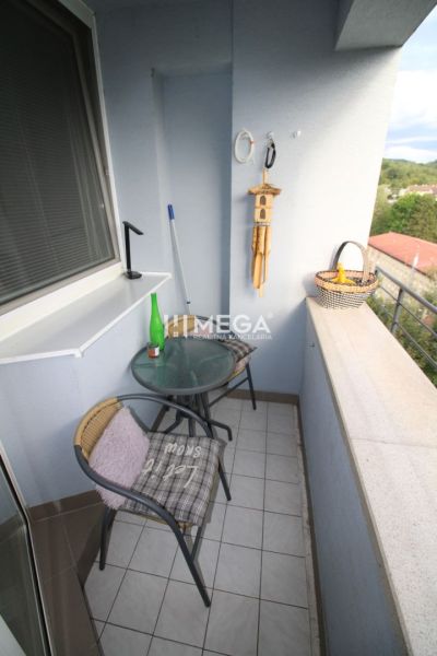 A balcony of a 2-room apartment with a café table and a view of greenery.