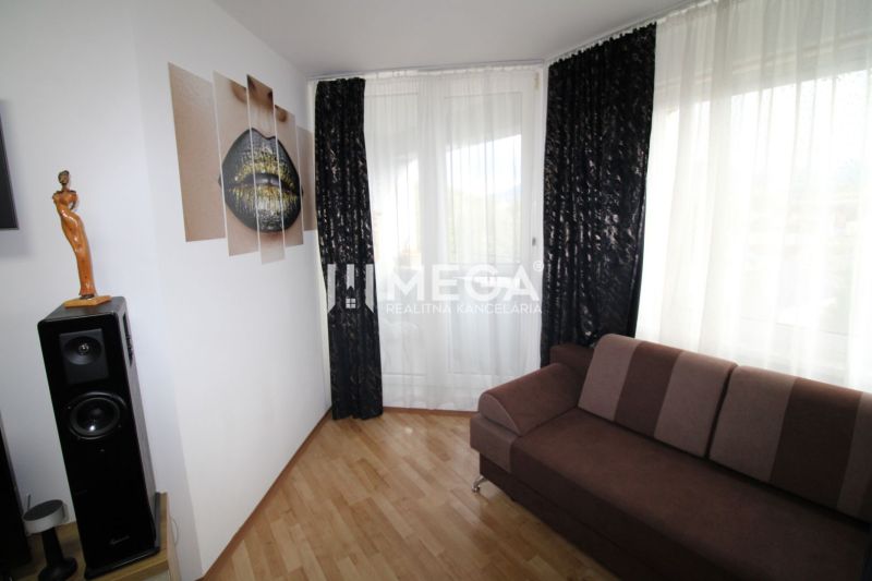 Living room in a two-room apartment with a dark sofa, speaker, and wooden decor flooring.