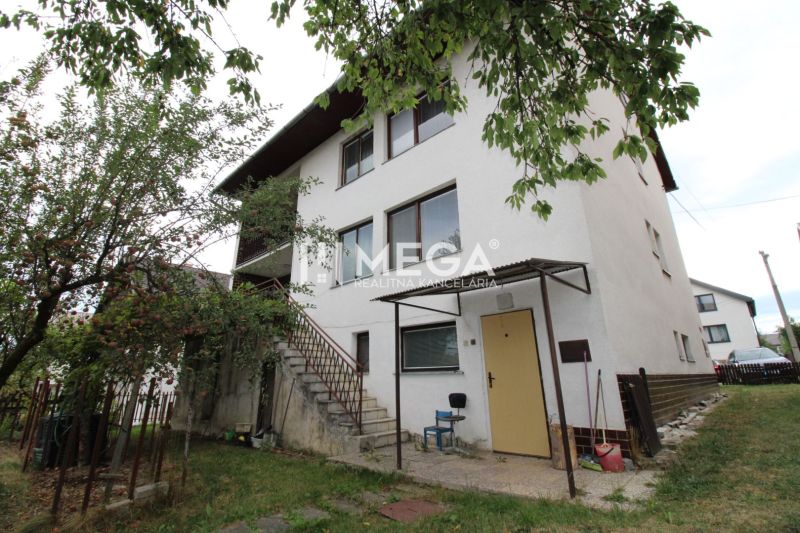 A family house on a street in Snina with two floors, trees, and an outdoor staircase.