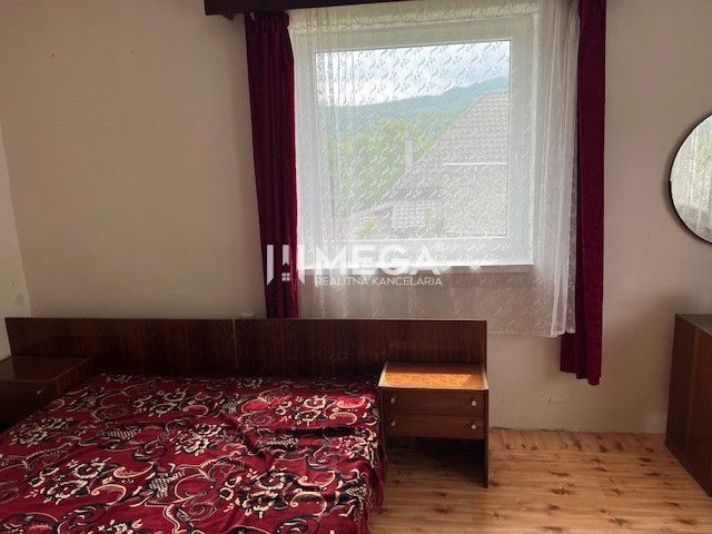 Bedroom in a family house with a bed, window, red curtains, and a wooden decor floor.