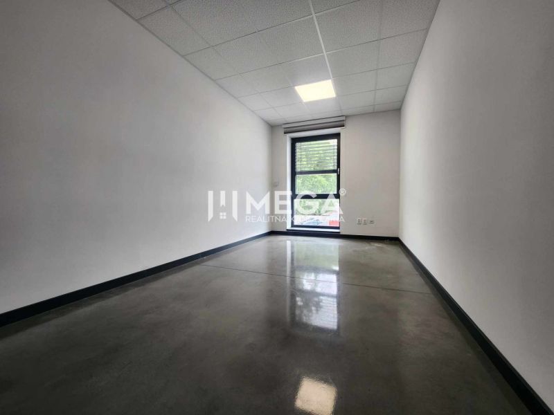 The interior of an office with a window, white walls, and a dark floor.