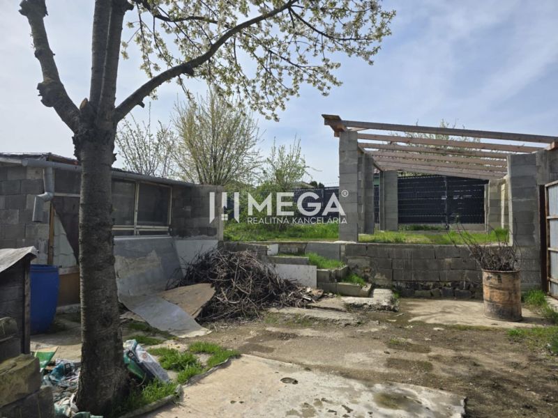 The courtyard of a family house in Sokoľany with a tree, building materials, and an unfinished structure.