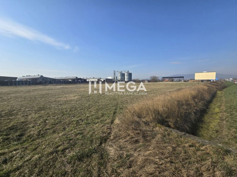 Grass and industrial premises in Hriadky under a clear sky, with an industrial building on the horizon.