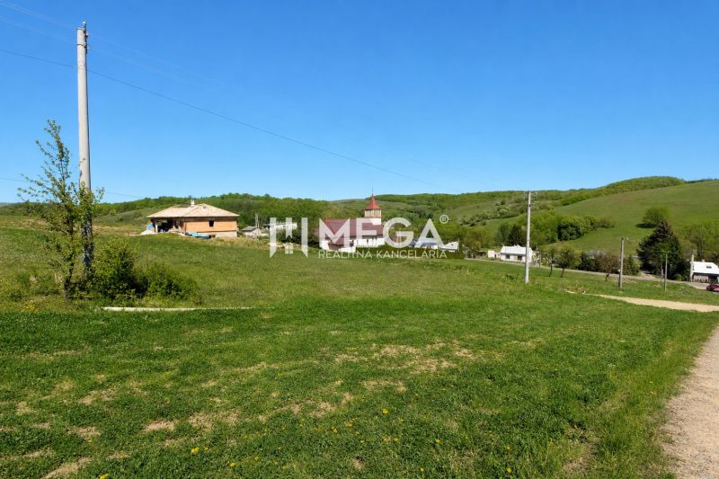 Grassy residential plots in the village of Víťazovce surrounded by green hills and buildings.
