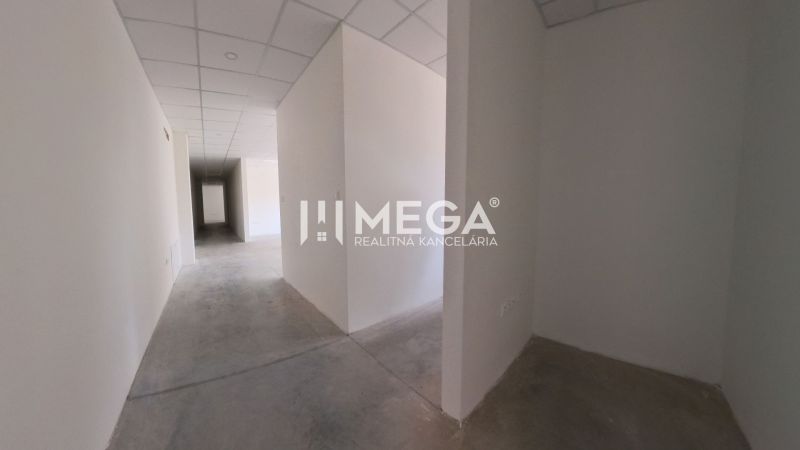 A hallway in an office with white walls, concrete flooring, and a drop ceiling.