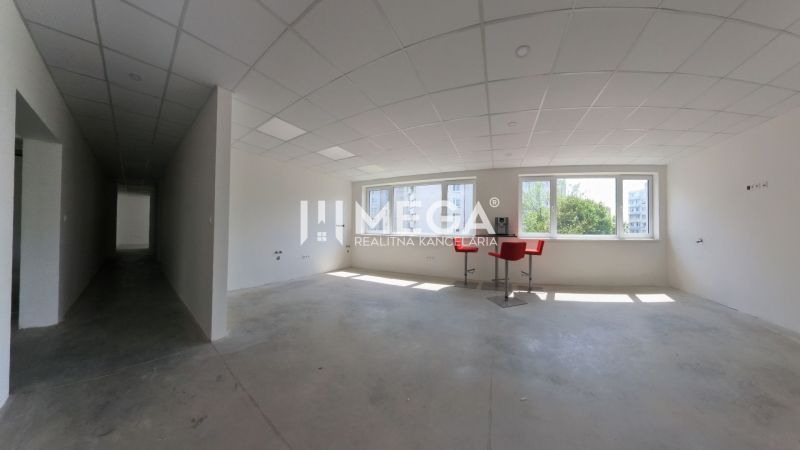 A bright office with white walls, ceiling panels, and red chairs by the windows.