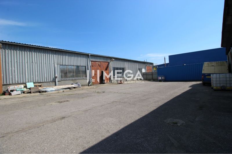 Warehouses and halls on Fidlikova Street in Humenné with stored material and a parked car.