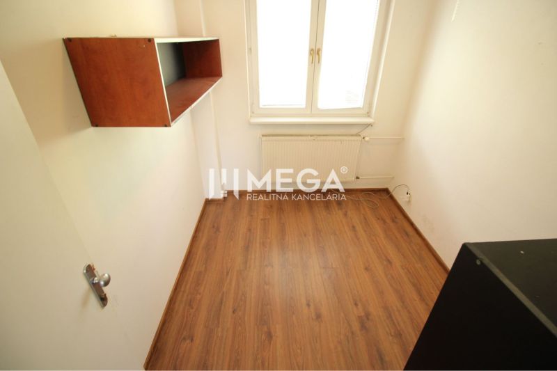 A small office with a shelf, a wooden decor floor, and a radiator under the window.