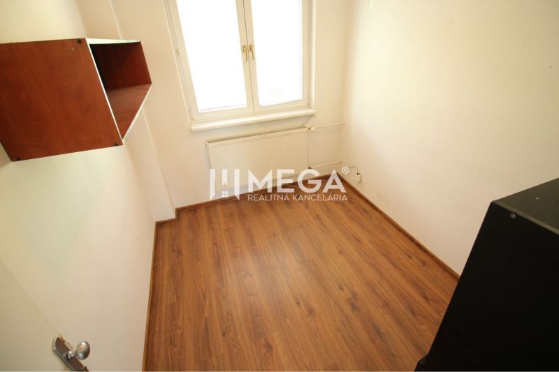 Small office with a shelf, wooden-patterned floor, window, and radiator.