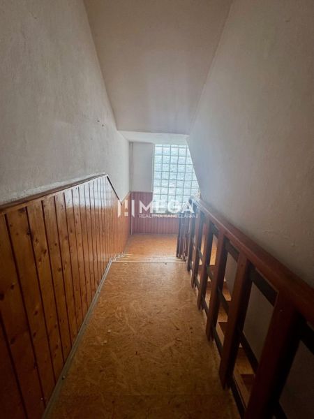 A hallway with wooden paneling and railing, a floor with a wooden decor, a window made of glass blocks.