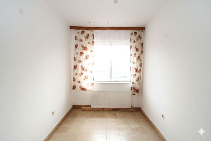 A room in a family house with a window, floral curtains, and tiles.