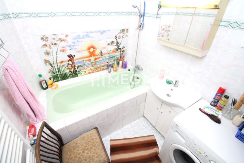 Bathroom with a green bathtub and a washing machine in a family house, tropical landscape decoration on the tiles.
