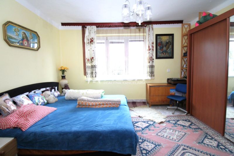 A bedroom in a family house with a blue bed, wooden furniture, and a colorful carpet.