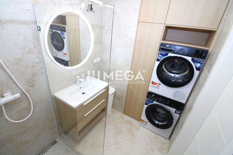 A bathroom in a 3-room apartment with a washing machine, dryer, and illuminated round mirror.
