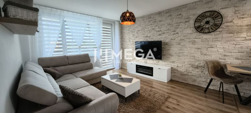 Living room in a 3-room apartment, with a wooden decor floor and a TV on a stone wall.