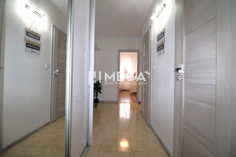 A hallway with ceramic tiles in a 3-room apartment with white walls and light-colored doors.