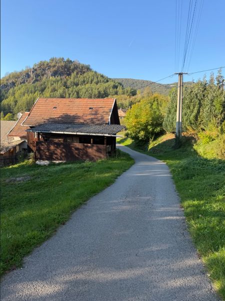 The road in Košecké Podhradie runs alongside houses, bordered by greenery and hills. Plots - residential.
