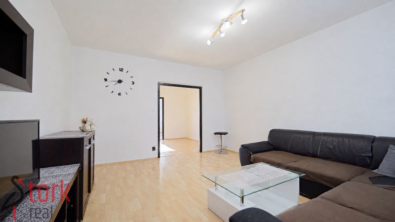 Living room in a three-room apartment with a sofa, glass table, and wooden decor flooring.