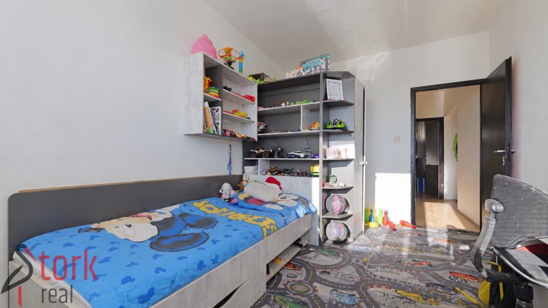 A children's room in a 3-room apartment with a bed and shelves full of toys and books.