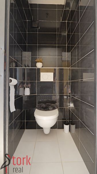 A bathroom in a three-room apartment with dark gray tiles and white sanitary ware.