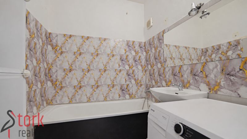 A bathroom with a bathtub and a washing machine in a 3-room apartment, tiles with a bold pattern.