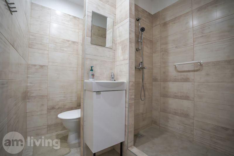 Bathroom in a studio apartment with a sink, shower, and beige tiles.