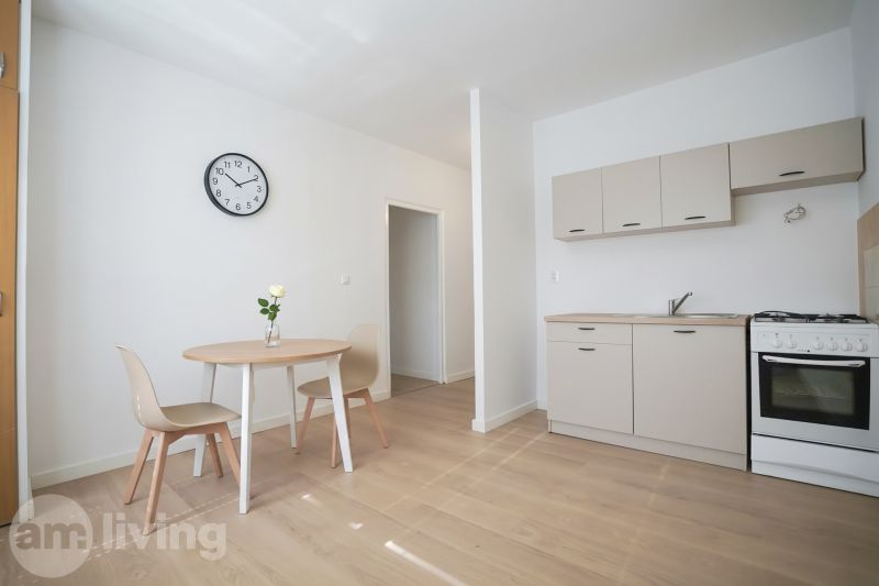 A kitchen in a one-room apartment with a wooden decor floor, a dining table, and a clock.