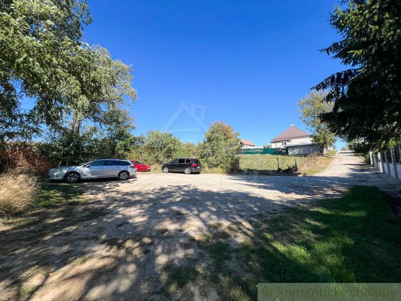 Cars are parked on a paved area near the gardens in Pastuchov under a clear blue sky.