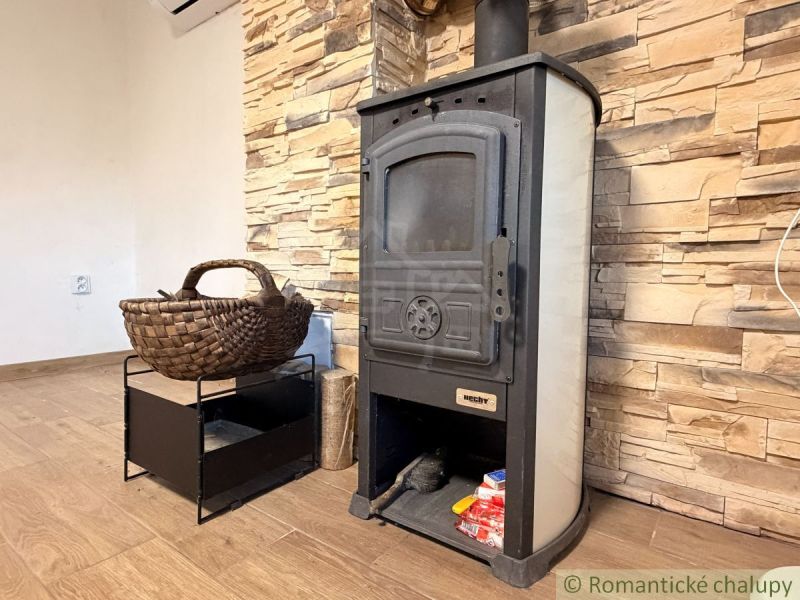 Wood-burning stove with a woven basket and a stone wall, floor with wooden decor in the cabin.