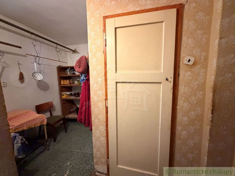 Interior of a family house with a hallway, a chair, and shelves. Kitchen tools are hanging here.