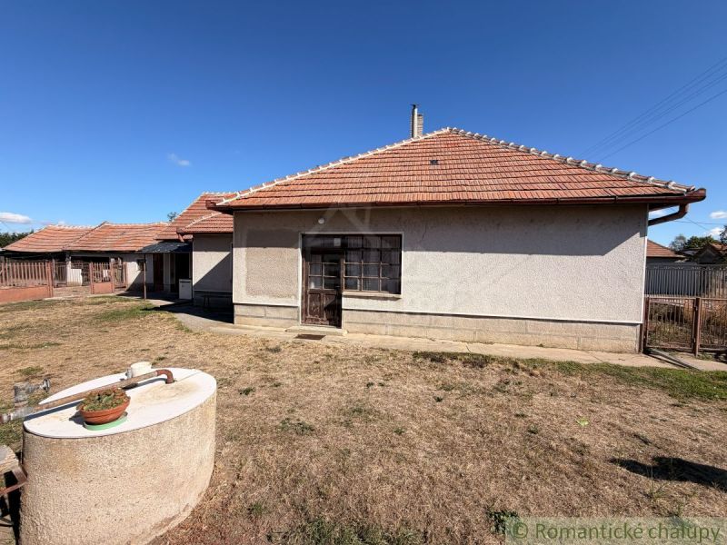 A family house in Hurbanovo with a sloped roof, a well, and sparse grass around.