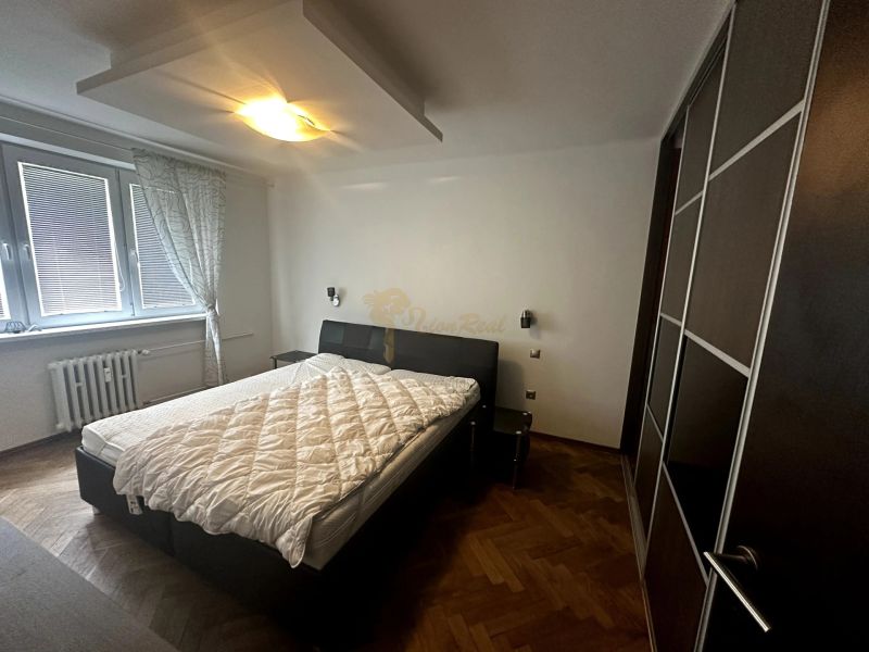 Bedroom in a two-room apartment with a bed, wardrobe, and wooden decor flooring.