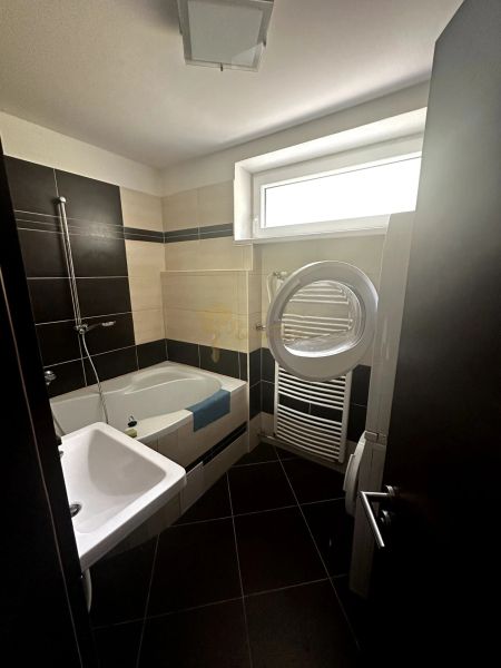Bathroom in a 2-room apartment with a bathtub, sink, and washing machine; black and beige tiles.
