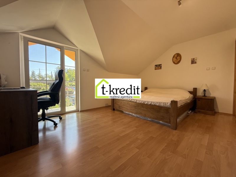 Attic bedroom in a family house with a bed, wooden decor flooring, and a desk.
