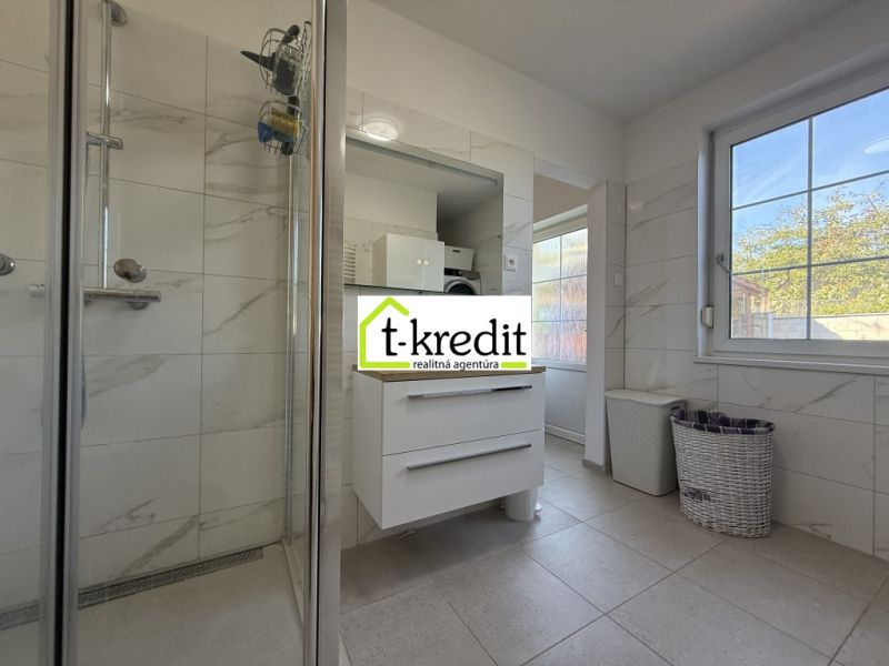 A bathroom in a family house with white tiles, a shower, and storage spaces.
