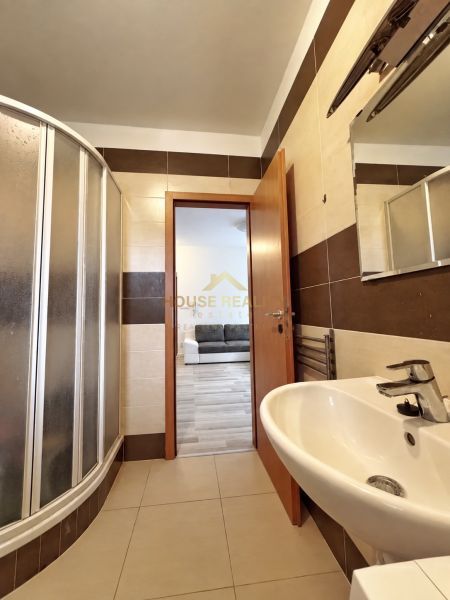 A bathroom in a studio apartment with a sink, a shower corner, and brown-beige tiles.